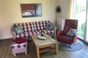 Ein Wohnzimmer mit grau-kariertem Sofa, einem roten Sessel, einem Holztisch und einem Gemälde an der Wand.