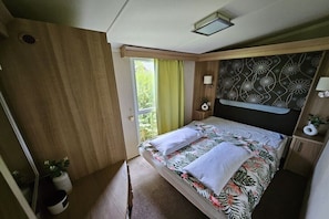 Ein Schlafzimmer mit einem Bett, einem Fenster mit Vorhängen, einem Nachttisch und einer Wand mit einem Blumenmuster.