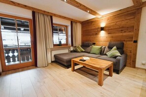 Ein gemütliches Wohnzimmer mit einer Couch, einem Holztisch und einem Fenster mit Vorhängen.