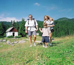 Eine Familie geht auf einem grasbewachsen Pfad, im Hintergrund ist ein kleines Gebäude zu sehen.