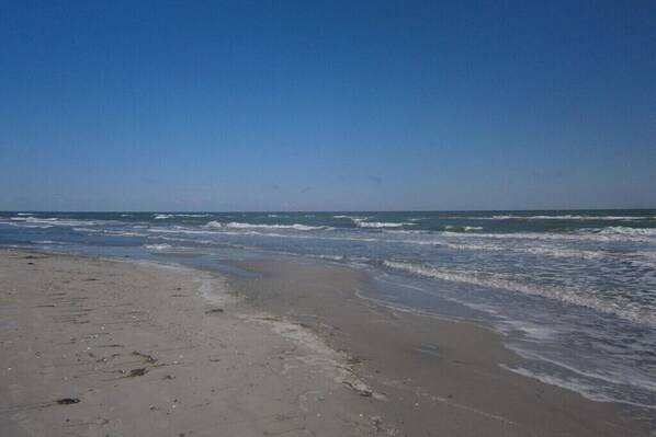 Ein Strand mit Wellen, blauem Himmel und Fußspuren im Sand.