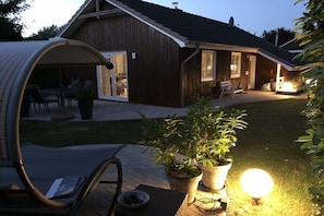 Ein Holzhaus mit überdachter Terrasse, Blumentöpfen und einem gut beleuchteten Außenbereich.