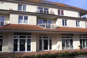 Ein mehrstöckiges Gebäude mit Balkonen und Geschäften. Auf den Schaufenstern stehen die Schilder 'Appartementvermietung', 'It Der Hot', 'Siggelkow' und 'Freizeit'.