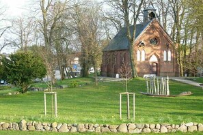 Eine Kirche mit einem Glockenturm, umgeben von einer Steinmauer und einer begrünte Fläche mit Bäumen.