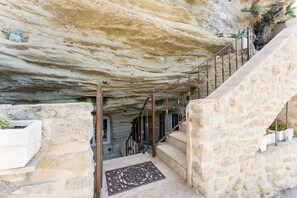 A stone staircase leading to a cave entrance, with a metal railing and a doormat at the bottom.