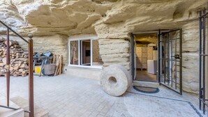Un edificio de piedra con una entrada rústica, una gran piedra molendera y un montón de leña.
