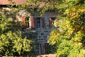 Ein Steinhaus mit roten Fensterläden, umgeben von viel Grün.