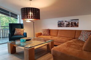 A modern living room with a glass coffee table, a sofa, a chair, and a pendant light. - Holiday apartment with 2 bedrooms (Bad Kohlgrub)