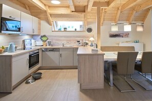 Eine moderne Küche mit Holzbalken, einer Essecke mit zwei Stühlen, einem Einbauofen und einem Fenster über der Spüle.