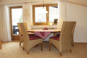 Un comedor con una mesa de madera, sillas de mimbre con cojines rojos, un mantel con diseño de alce y una ventana con cortinas.