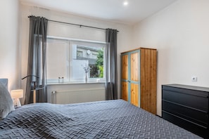 Ein Schlafzimmer mit Bett, Kleiderschrank, Heizkörper und einem Fenster mit Vorhängen.