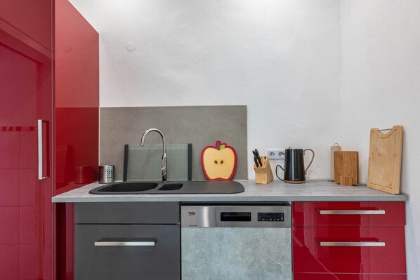 Una cocina moderna con lavavajillas, pileta doble y muebles colorados.
