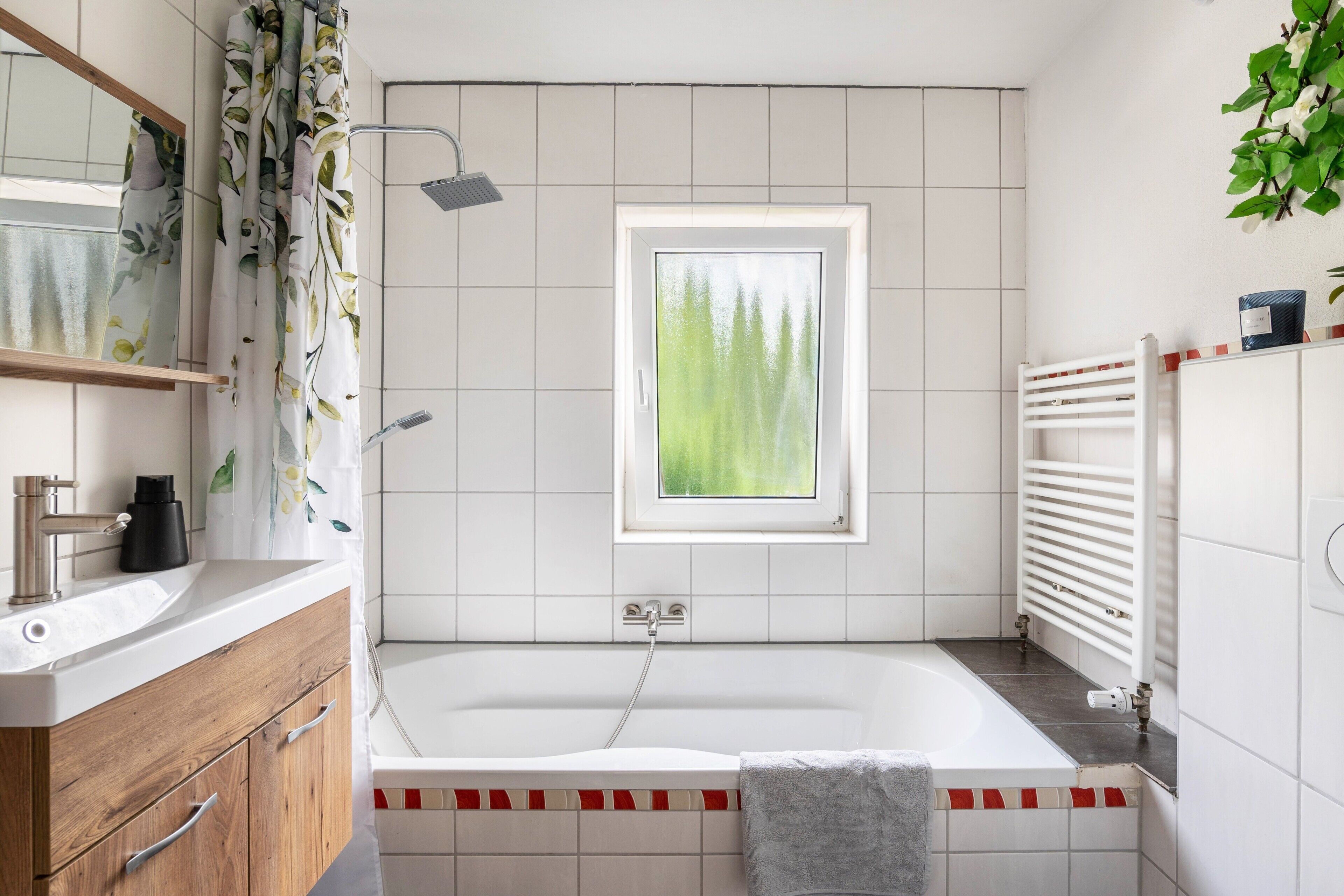 A modern bathroom with a bathtub, a shower, a window with a view, and a white tiled wall.