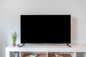 Ein Flachbildfernseher auf einem weißen Ständer mit einer kleinen Pflanze und einer Fernbedienung daneben.