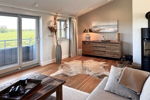 A spacious living area with a large window, a wooden coffee table, a sofa, a fireplace, and a rustic rug. - Penthouse House Hemingway (Rosenhagen)