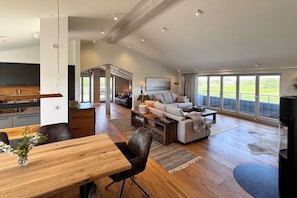 A spacious living area with a dining table, sofa, and large windows offering a view of the outdoors. - Penthouse House Hemingway (Rosenhagen)