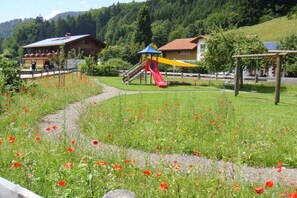 Ein Spielplatz mit Rutsche und Klettergerüst, umgeben von einer Wiese mit Mohnblumen.