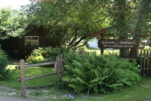 Ein Holzschild mit Schriftzug, eine Holzzaun und üppiges Grün.