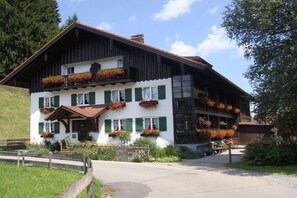 Ein traditionelles Chalet mit geneigtem Dach, mehreren Balkonen mit Blumenkästen und einem Eingang mit Stufen.