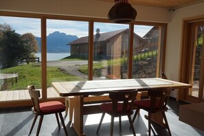 Ein Essbereich mit großem Tisch und Stühlen, große Fenster mit Blick auf einen See und Gebäude.