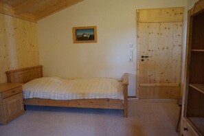A bedroom with a wooden bed, a nightstand, a wooden wardrobe, and a door with a small picture on the wall.
