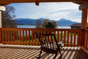 A wooden deck with a rocking chair, overlooking a lake and mountains.