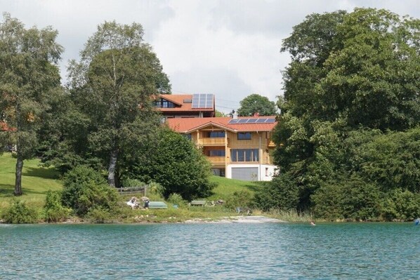 Ein mehrstöckiges Gebäude mit Solaranlage, umgeben von Bäumen und einem Gewässer.