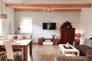 Een woonkamer met een houten plafond, een flatscreen-tv, een kast, een bank en een eettafel met stoelen.