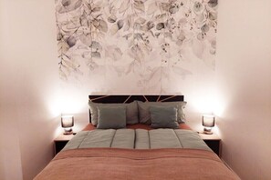 Ein Schlafzimmer mit einem Bett, Kissen, Nachttischlampen und einer Wanddekoration mit Blumenmuster.