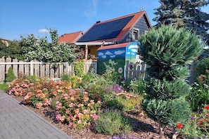 Ein Haus mit Solardach, einem Garten mit unterschiedlichen Pflanzen und einem Holzzaun.