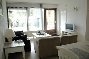 A room with a bed, a desk, a chair, a television, and a window with blinds. - Holiday apartment with 1 bedroom (Petten)