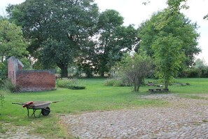 Un jardin avec une brouette, une construction en briques et une zone pavée.
