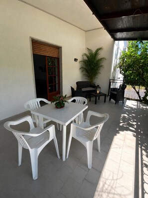 Un patio con una mesa y sillas blancas, una planta en maceta y una puerta de madera.