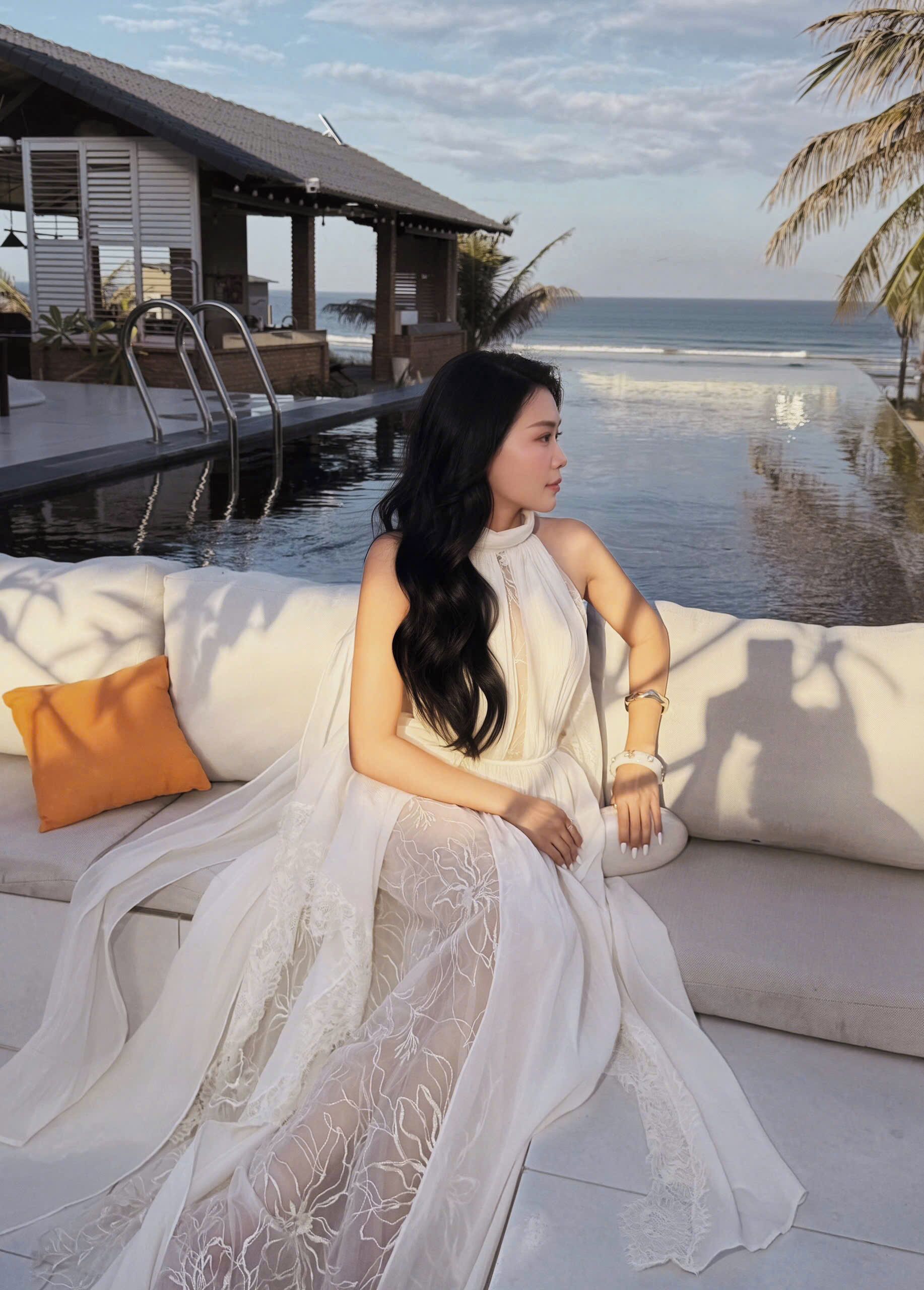 Eine Person sitzt auf einer weißen Außensofa mit Blick auf einen Pool und das Meer.