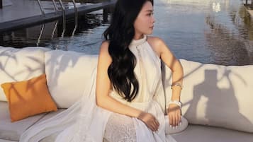 A person seated on a white outdoor sofa with a view of a pool and the sea.