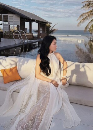 Una persona sentada en un sofá blanco al aire libre, con vista a una piscina y al mar.