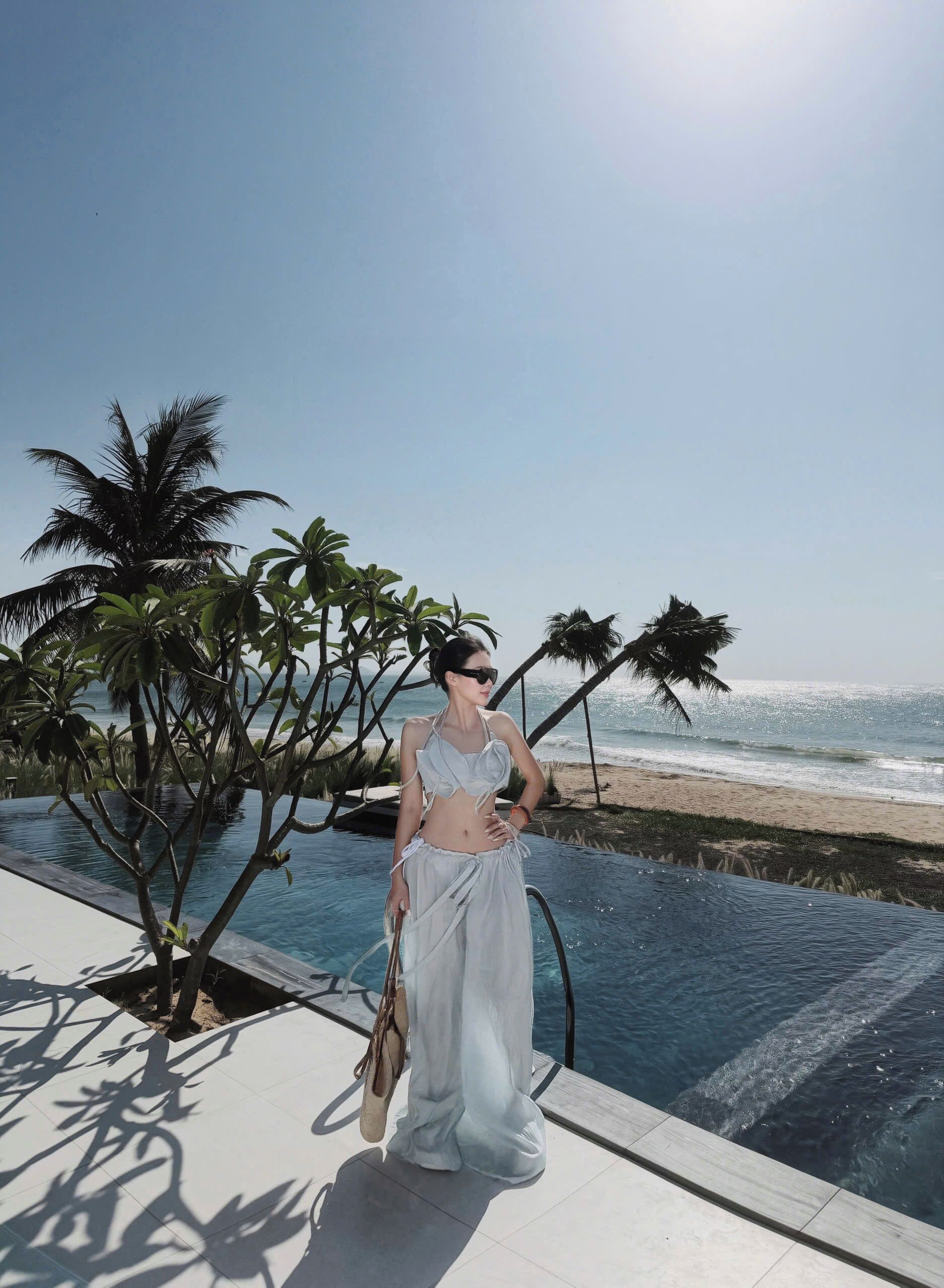 A person standing by a pool with a view of the ocean and palm trees.