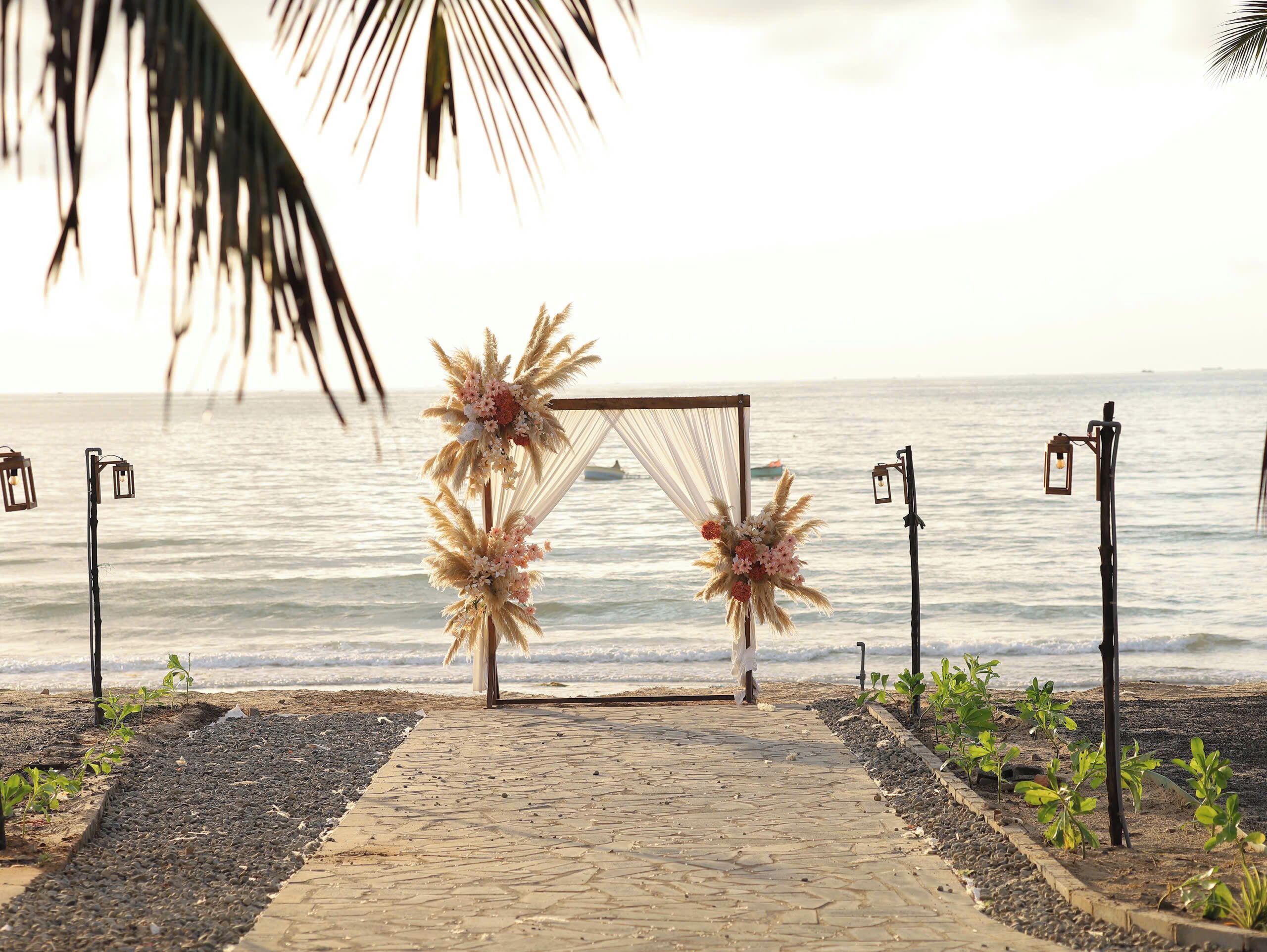 Un arco nupcial frente al mar, con un sendero decorado con flores y plumas de pampa.