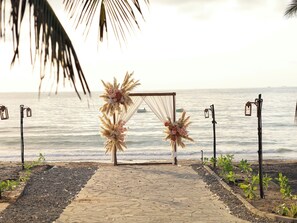 A beachside wedding arch with a pathway leading to it, decorated with flowers and pampas grass.