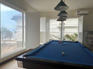 Una mesa de billar con una bola, una lámpara colgante y vistas al exterior.
