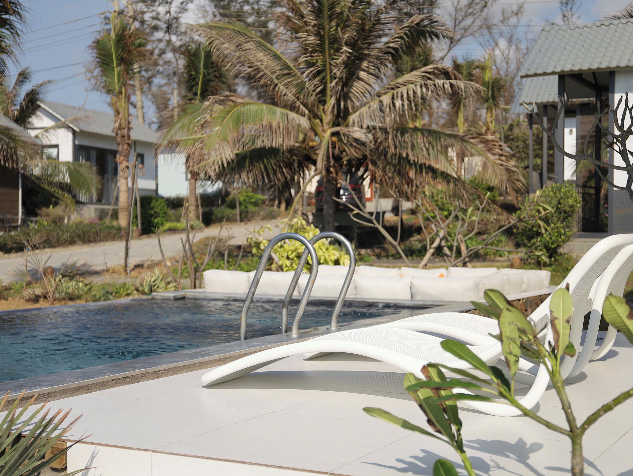 A swimming pool with a metal ladder, white lounge chairs, and palm trees in the background.