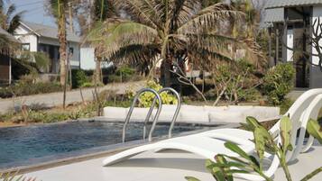 A swimming pool with a metal ladder, white lounge chairs, and palm trees in the background.