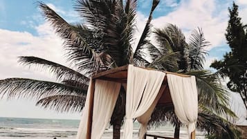 A beachside bed with a canopy, a pool, and palm trees.