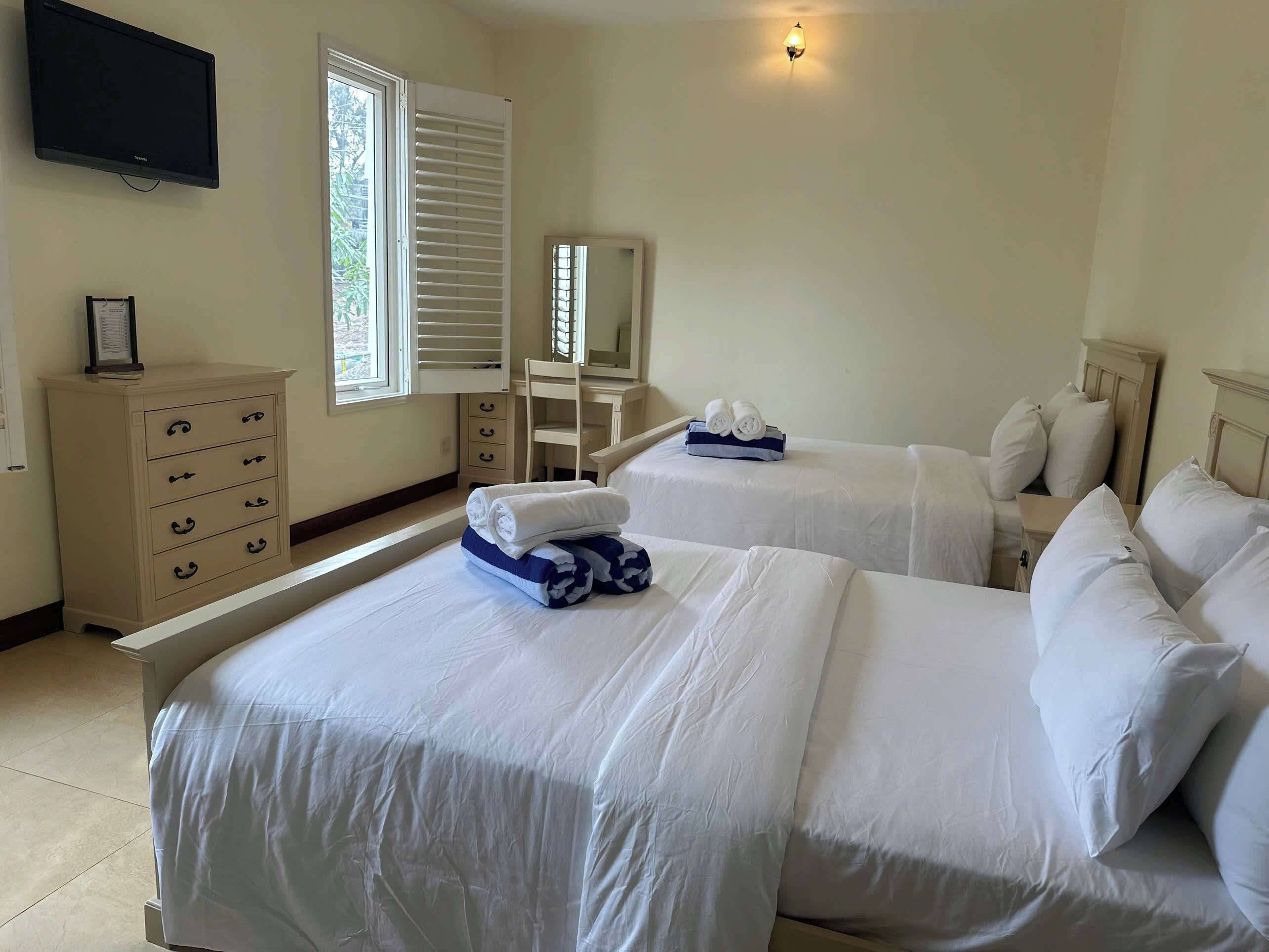A hotel room with two beds, a dresser, a chair, a desk, and a television.