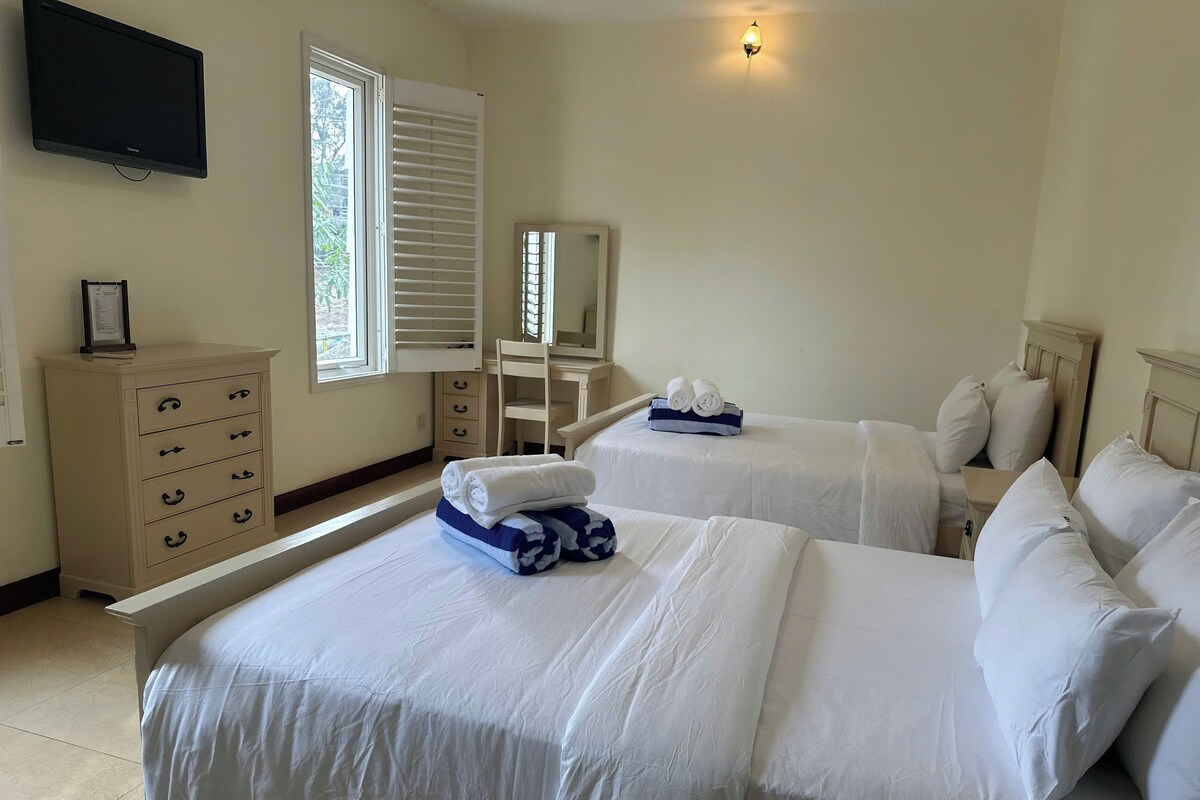 A hotel room with two beds, a dresser, a chair, a desk, and a television.