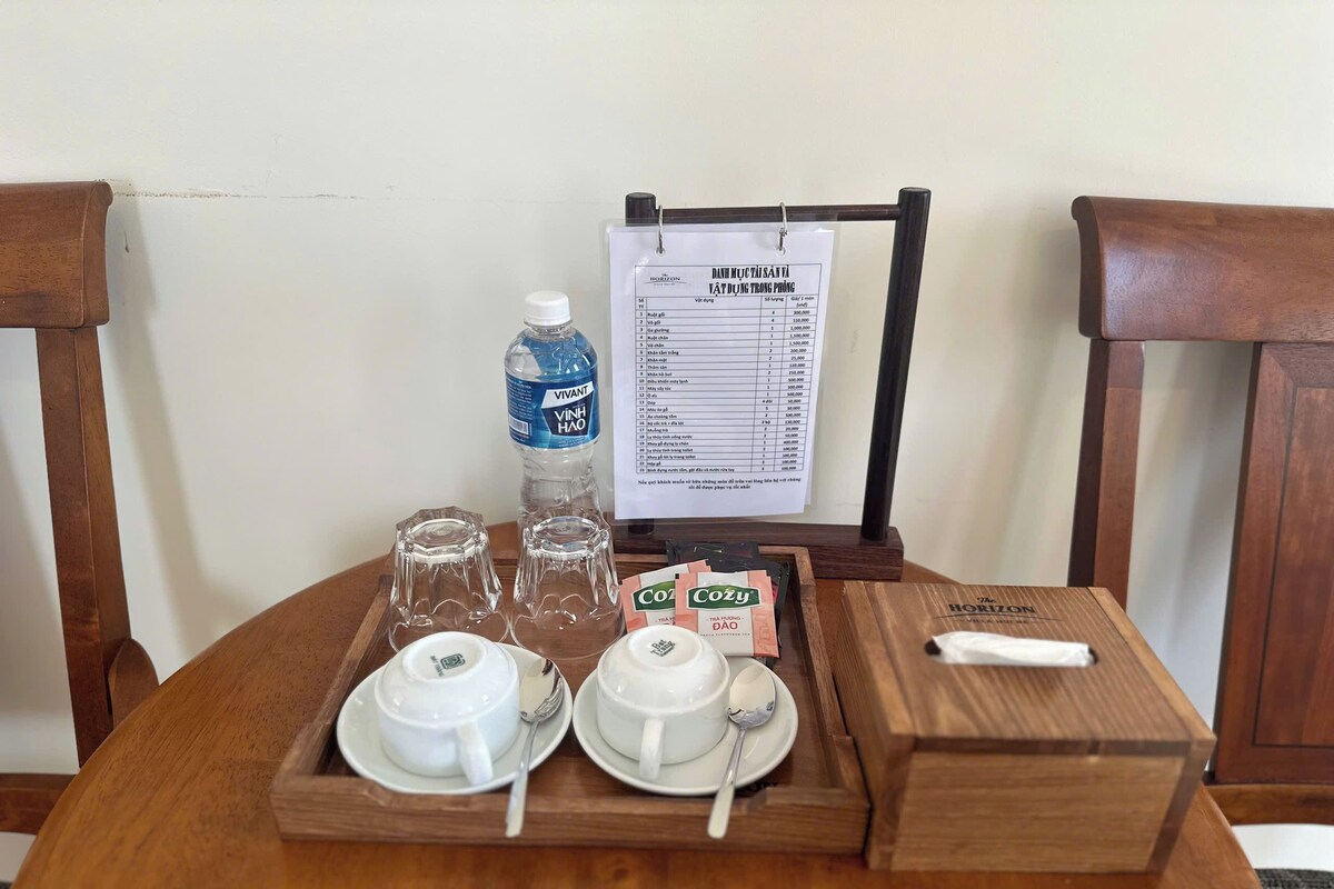 A wooden table with a tray containing two white teapots, two teacups, two spoons, a bottle of water, and a menu.
