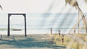 A beach with a swing set, palm trees, and a clear view of the ocean.