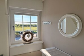A room with a window, a round mirror, a wall-mounted light fixture, and a decorative wreath. - Beach House Holiday Home 1 (Sylt\/ Westerland)