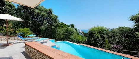 A swimming pool with a stone wall and blue lounge chairs.