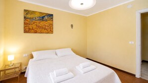 Hotellihuone, jossa on sänky, taulu, yöpöytälamppu ja ovi.